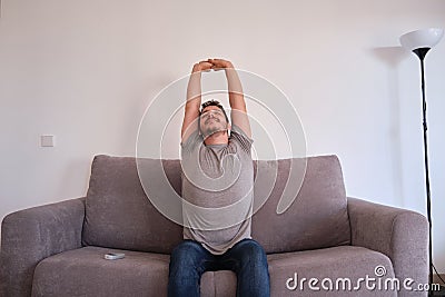 Portrait of a smiling young man sitting on a sofa stretching after a productive and long day Stock Photo