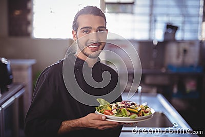 Portrait of smiling young waiter holding salad plate at commercial kitchen Stock Photo