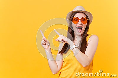 Portrait of smiling young woman in straw summer hat, orange glasses pointing index fingers aside copy space isolated on Stock Photo