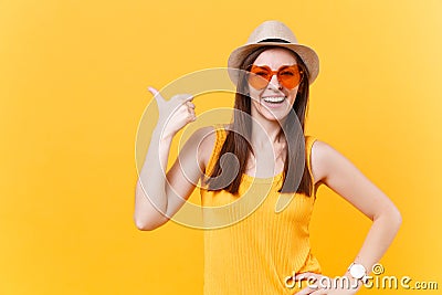 Portrait of smiling young woman in straw summer hat, orange glasses pointing right hand aside copy space isolated on Stock Photo