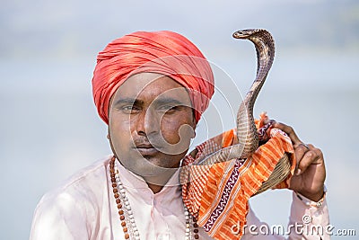 Portrait snake charmer adult man in turban and cobra sitting near the lake. Pokhara, Nepal Editorial Stock Photo