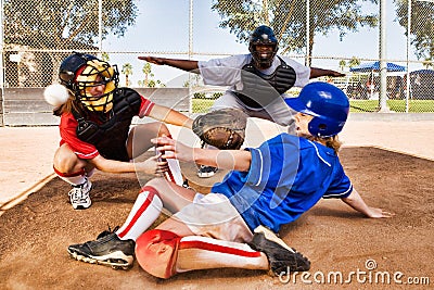 Portrait of Softball player sliding into home plate while umpire rules safe Stock Photo