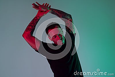 Portrait of sport fit attractive man making arm stretch. Masculine, tattooed hands, hipster look. Color flash studio light. Stock Photo