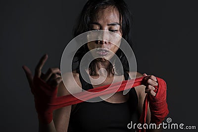 Portrait of sporty and fit fighter Asian Chinese woman using wrist wraps wrapping before mma fight sport or boxing workout looking Stock Photo