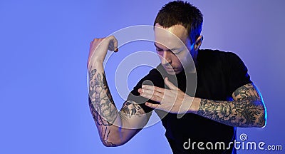 Portrait of sporty fitness man showing muscular triceps, tattooed hands, hipster. Color flash studio light. Stock Photo