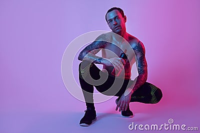 Portrait of sporty fitness man sitting with bottle of water, tattooed hands, hipster. Color flash studio light. Stock Photo