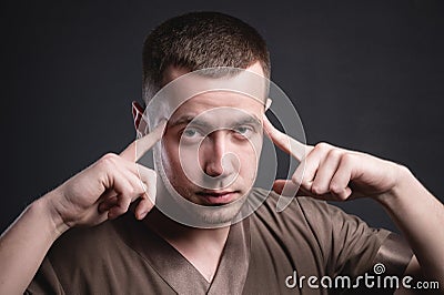 Portrait of a strong and large male masseur in special clothes with a finger at the temple reads your thoughts and knows Stock Photo