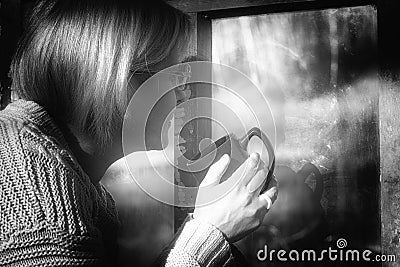 Artistic portrait of a woman looking out of the window to the street. He holds a mug with a drink in his hand Stock Photo