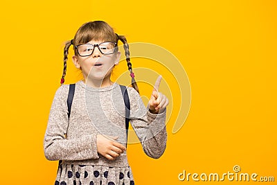Portrait of stylish child girl pointed finger up. Little child in glasses has idea. Kid isolated on yellow background Stock Photo