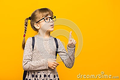 Portrait of stylish child girl pointed finger up. Little child in glasses has idea. Kid isolated on yellow background Stock Photo