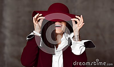 Portrait of stylish high-society lady in black jacket and white shirt pulling down hat brim hiding her eyes and laughs Stock Photo