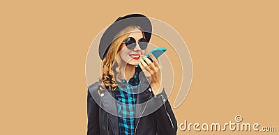 Portrait of stylish smiling young woman holding smartphone using voice command recorder, assistant or takes calling wearing black Stock Photo