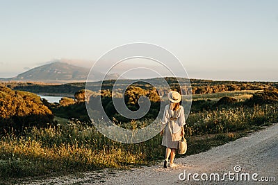 Portrait of a stylish woman walking with a straw bag through the field at sunset Stock Photo