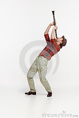 Portrait of stylish young man in red checkered shirt and hat playing clarinet isolated over white background. Classic Stock Photo