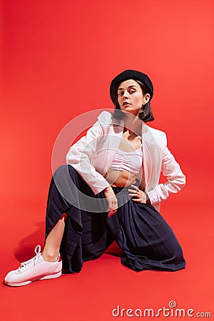 Portrait of stylish young woman in beret and jacket posing isolated over red studio background. Parisian outfit Stock Photo