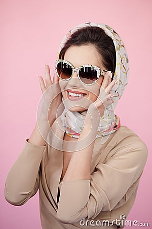 Portrait of a young woman wearing elegant clothes, sunglasses, he touches his glasses with his hands, pink background Stock Photo