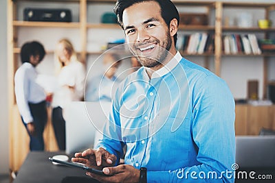 Portrait of successful confident hispanic businessman using tablet in the hands and smiling at camera in modern office Stock Photo