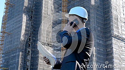 Portrait of a successful young handsome engineer, architect, builder, businessman, wearing a white helmet, in a suit, holding a pr Stock Photo