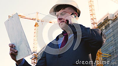 Portrait of a successful young handsome engineer, architect, builder, businessman, wearing a white helmet, in a suit, holding a pr Stock Photo