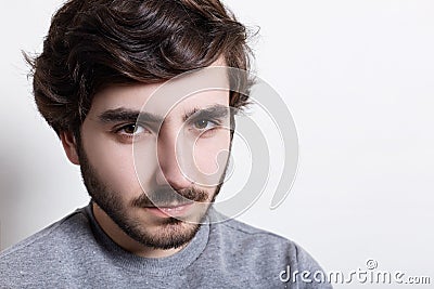 Portrait of sullen angry man with trendy hairstyle and dark beard wearing grey casual sweater looking at camera with serious and s Stock Photo