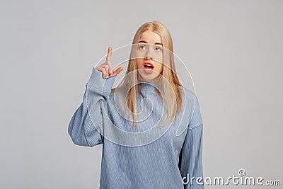 Portrait of surprised blond young woman in blue sweatshirt pointing finger and looking up with fascinated, impressed face Stock Photo