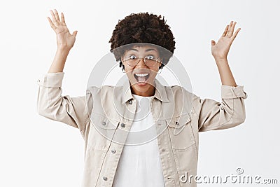 Portrait of surprised and impressed excited african american woman in glasses and beige shirt raising palms high in Stock Photo