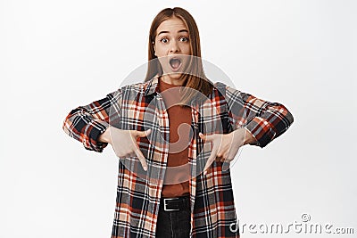 Portrait of surprised young woman gasp in awe, checking out big news, discounts and prices below, pointing down amazed Stock Photo