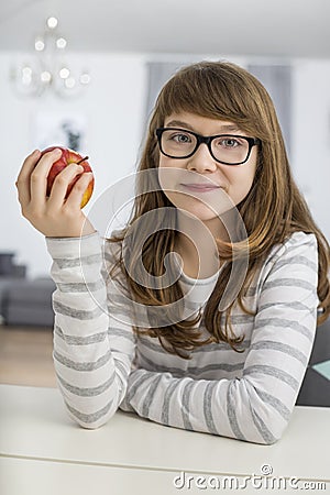 Portrait of teenage girl holding apple while sitting at table in house Stock Photo