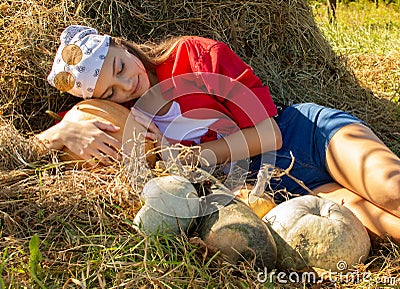 Teenage girl on a pile of hay with pumpkins in a red shirt and bandana Stock Photo