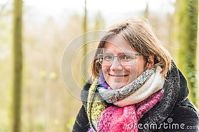 Portrait of a thirty year old white woman with a colorful scarf, glasses and a green bokeh nature background Stock Photo