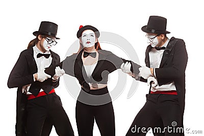 Portrait of three mime artists performing, on white background. Two men pull the girl to sides, can not divide Stock Photo