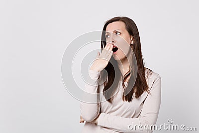 Portrait of tired boring young woman in light clothes looking aside, yawning covering mouth with hand on white Stock Photo