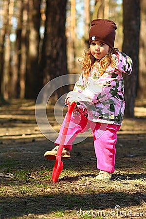 Portrait of a toddler girl digging the forest ground with a toy red shovel Stock Photo