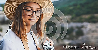 Portrait tourist girl in summer hat hold in hands retro camera and takes photos on backdrop of mountains landscape Stock Photo