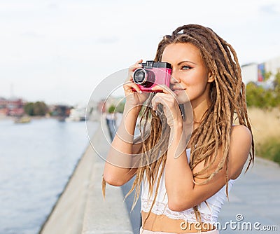 Portrait of Trendy Girl with Dreads and Vintage Camera Standing by the River. Modern Youth Lifestyle Concept. Take the picture. Stock Photo