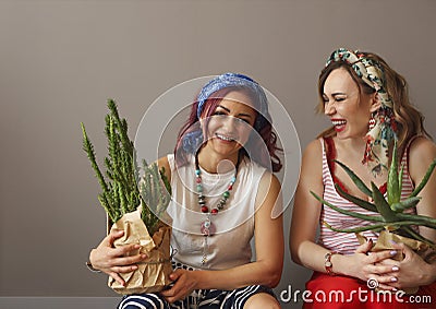 Portrait of two beautiful women in bright clothing and bow in head with bright lips holding cactuses Stock Photo