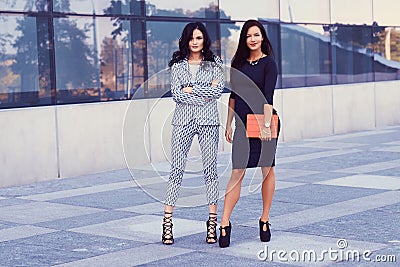 Portrait of two businesswomen dressed in a stylish formal clothes, standing in a downtown posing against a background of Stock Photo