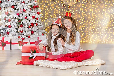 Portrait of two one young girls sisters close to white green Christmas tree. The girls in beautiful evening dresses clothes in New Stock Photo