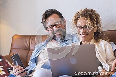 Portrait of two people man and woman enjoy technolofy connection toether with laptop and phone smiling and watching the computer Stock Photo