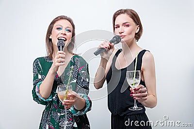Portrait of two singing girls with glasses in their hands. Karaoke concept Stock Photo
