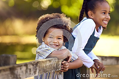Portrait Of Two Smiling Children Leaning On Fence On Walk In Countryside Stock Photo
