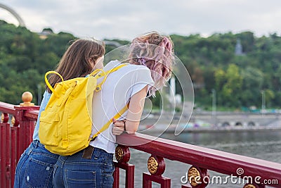 Portrait of two teenage girls standing with their backs on bridge over river Stock Photo