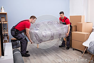 Male Movers Carrying Wrapped Sofa In New House Stock Photo