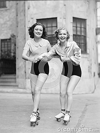 Portrait of two young women with roller blades skating on the road and smiling Stock Photo