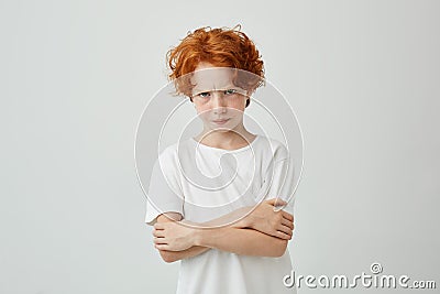 Portrait of unhappy red haired boy with freckles looking in camera with upset expression, crossing hands being Stock Photo