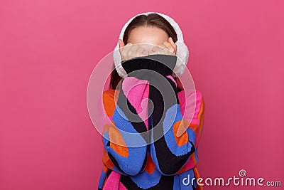 Portrait of unknown anonymous shy woman wearing winter earmuffs and warm sweater, covering her face with hands, hiding, posing Stock Photo