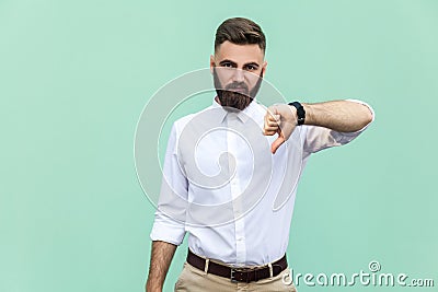Portrait of unsatisfied bearded man with thumbs down and white shirt against light green background. Stock Photo