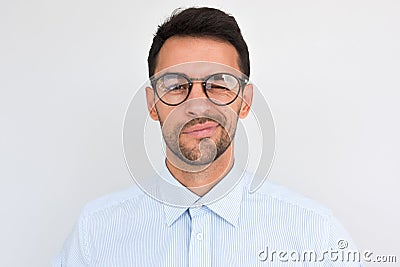 Portrait of unshaven handsome male frowns, being dissatisfied with something, blink with eye, wears round glasses and blue shirt, Stock Photo