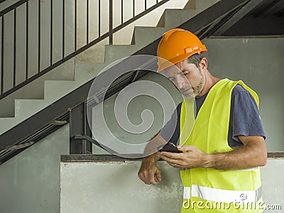 Portrait of upset construction worker or stressed contractor man in hardhat and vest checking on mobile phone unhappy in stress Stock Photo
