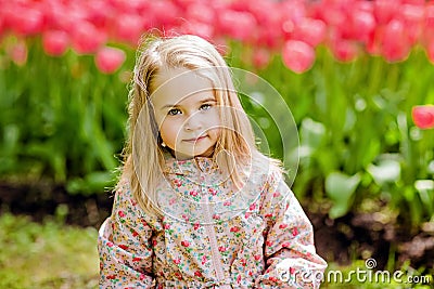 portrait of a very cute pretty girls blonde in a pink cloak around flower beds with red tulips in the Park Stock Photo